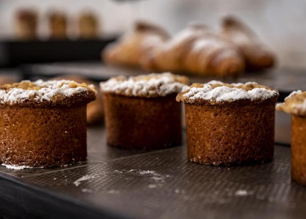 Baked pastries with powdered sugar, croissants in the background.